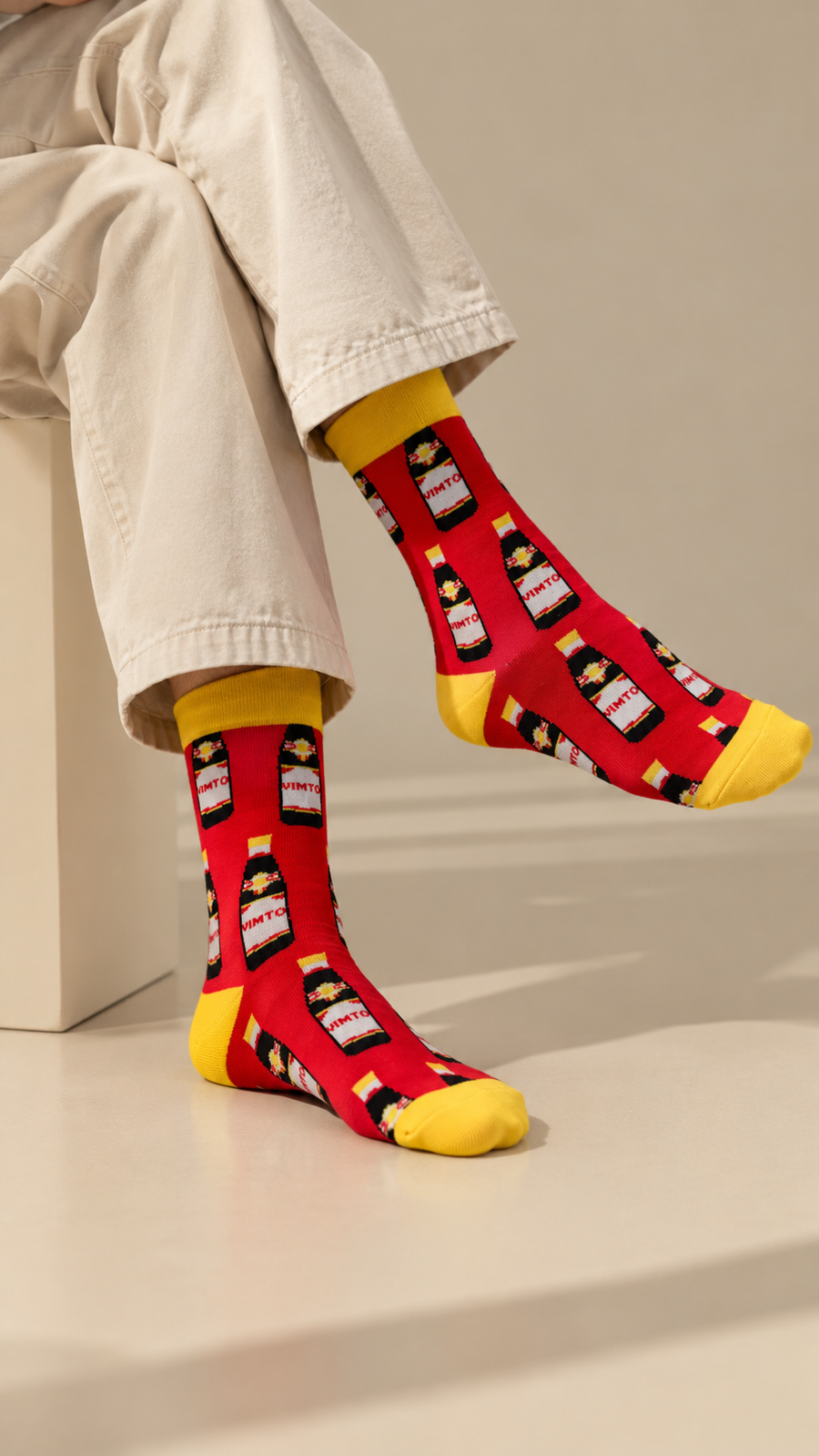 Vimto half crew socks by Socks Up, worn with cream trousers, seated