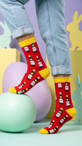 Person wearing red socks with yellow cuffs, featuring Vimto bottle pattern, styled.
