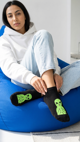 Woman wearing black socks with neon green alien designs, seated.