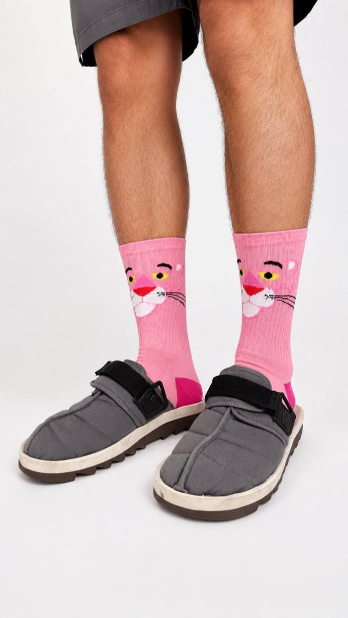 Pink Panther crew socks worn with grey quilted sandals and shorts, studio background